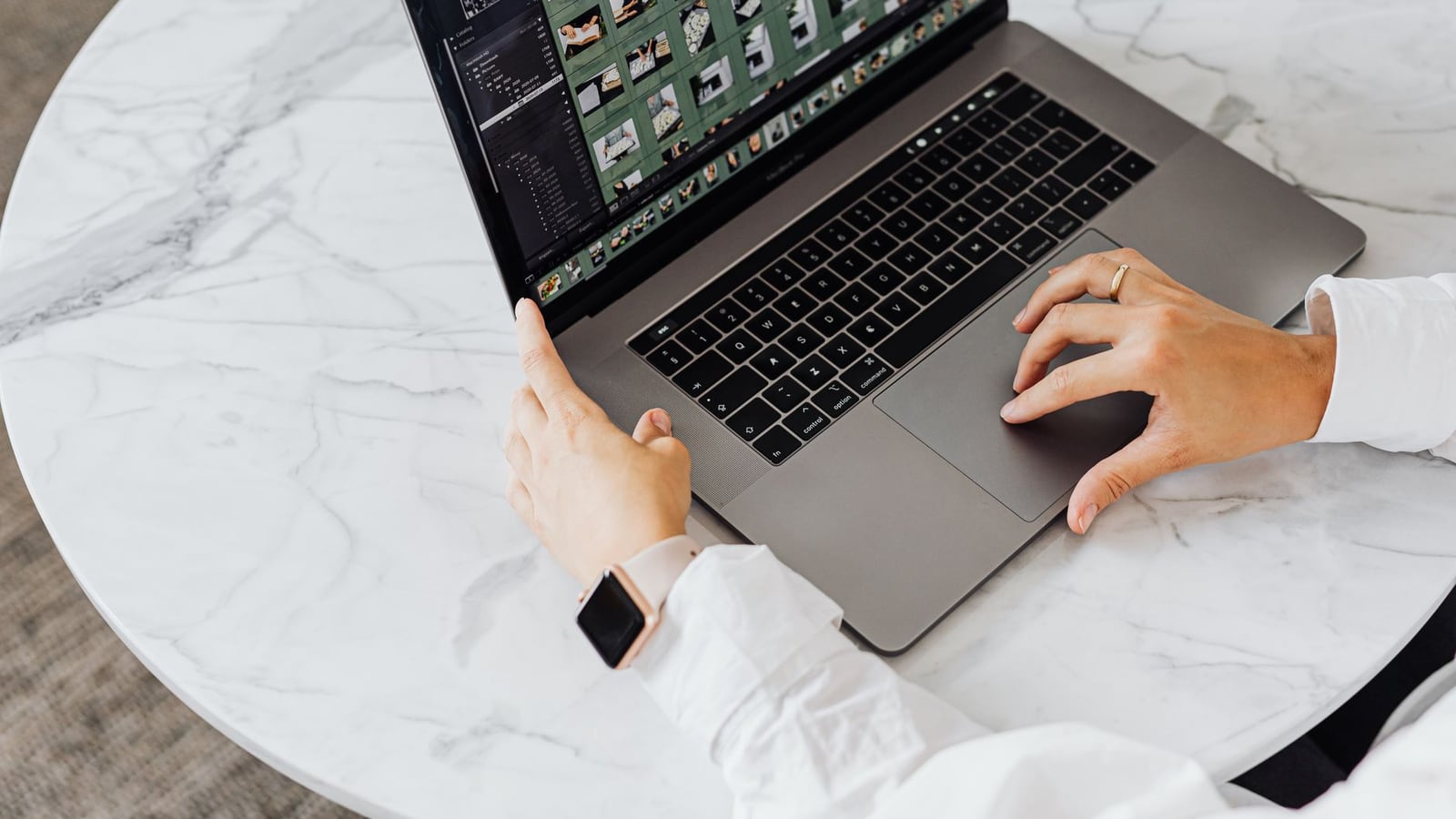 Hands editing photos on laptop, modern workspace on marble table.